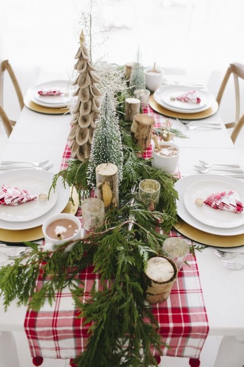 the table is set for christmas dinner with white plates and red checkered runneres