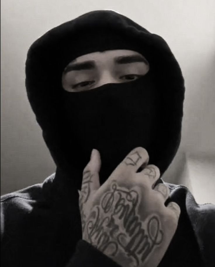 a man wearing a black hood and holding his hand up to his face with tattoos on it