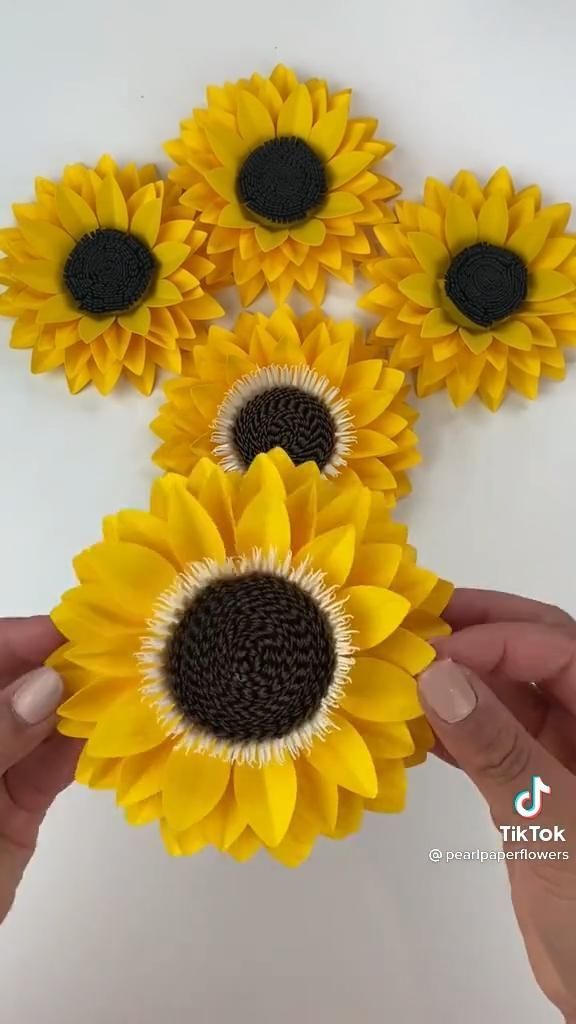 sunflowers made out of yarn are being held by someone's hands on a white surface