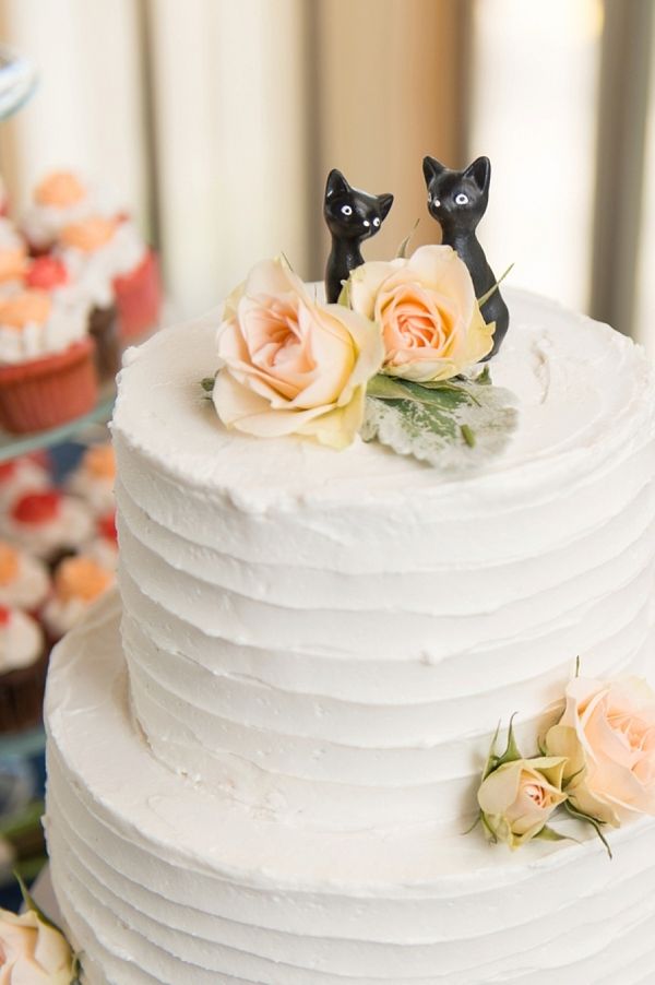 two cats figurines sitting on top of a white cake