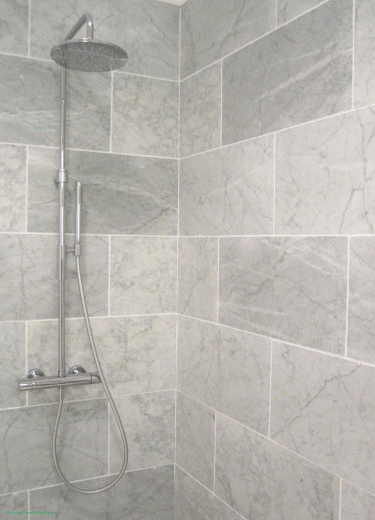 a walk in shower sitting next to a white tiled wall and floor with grey tiles