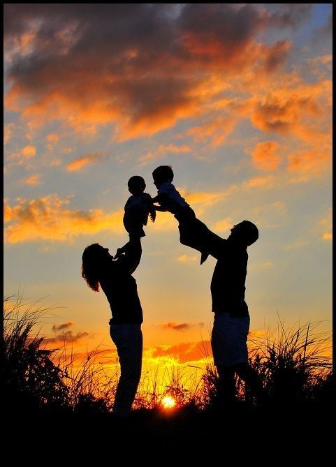 two adults and a child standing in front of a sunset