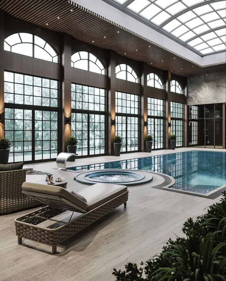 a large indoor swimming pool with sun loungers and chairs next to it, surrounded by tall windows