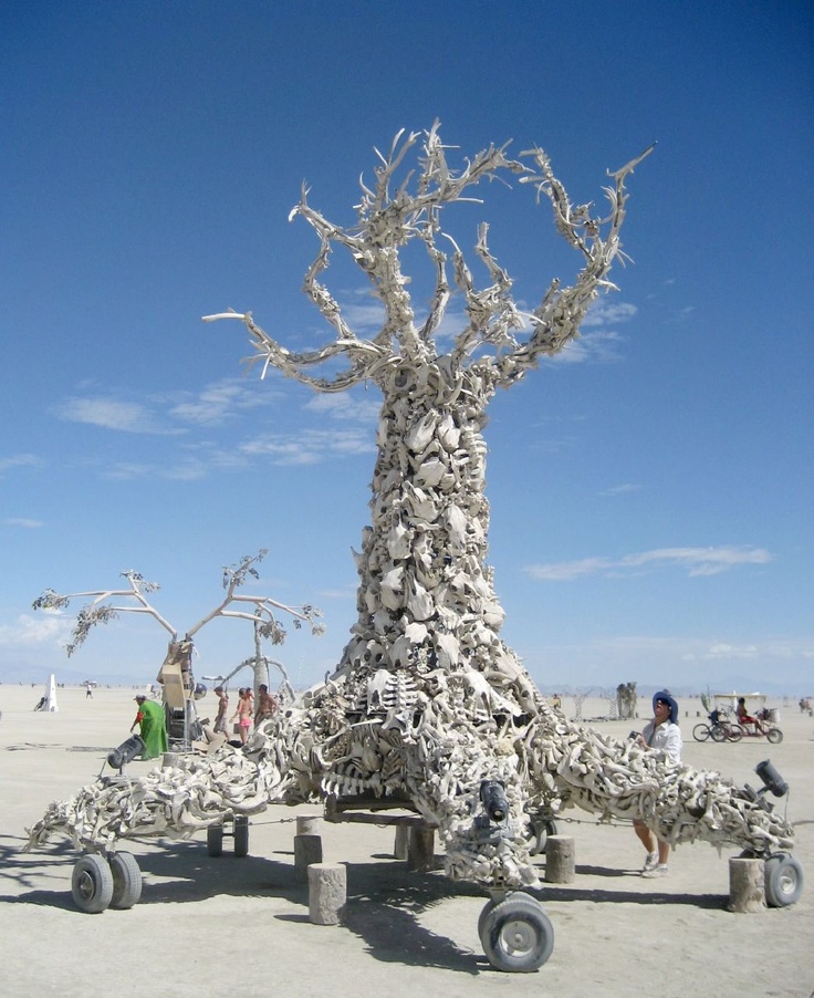 a sculpture made out of rocks and tires on the beach with people standing around it