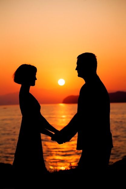 the silhouette of two people holding hands in front of an orange and yellow sunset over water