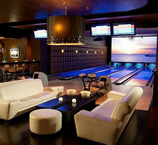 a bowling alley with couches, tables and chairs around it in front of a flat screen tv