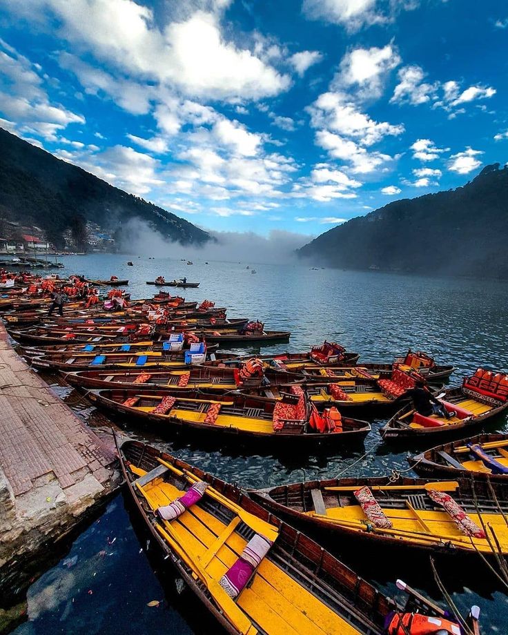 many boats are lined up on the water in front of some mountains and clouds above them