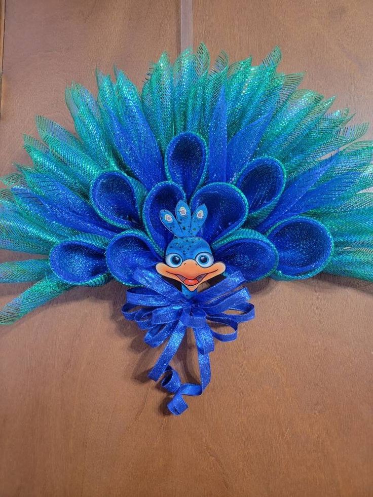 a blue and green peacock head with feathers on it's face, sitting on top of a wooden table