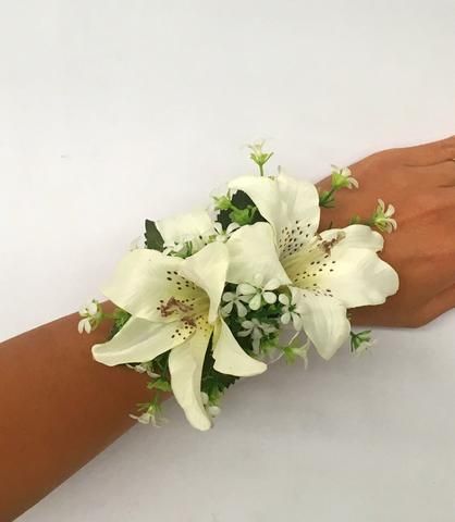 a woman's hand holding a bouquet of white lilies and greenery on her arm