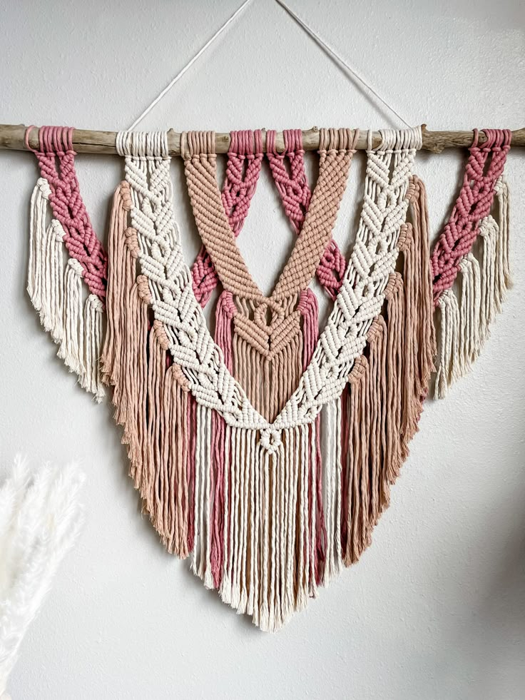 the wall hanging is decorated with pink, white and beige fringes on a wooden stick