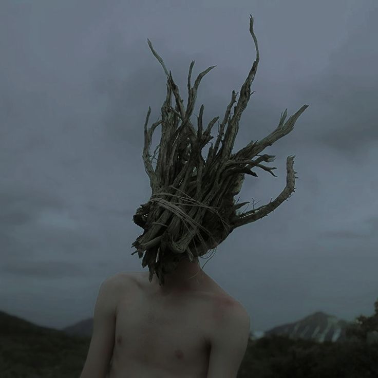 a shirtless man with branches on his head in the middle of a dark forest