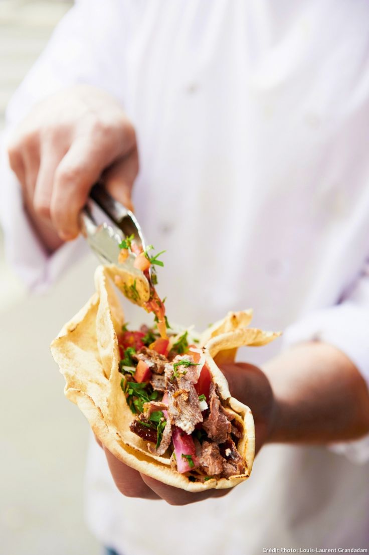 a person is holding a pita filled with meat and veggies while wearing a chef's coat