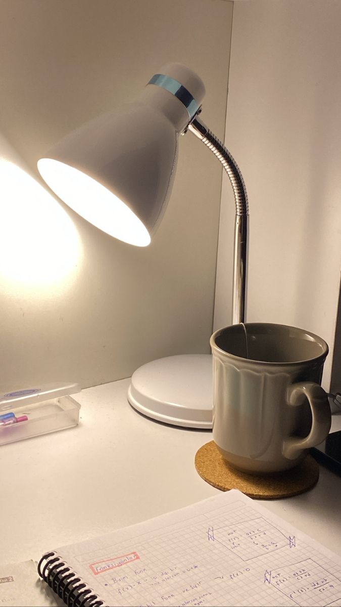 a desk lamp sitting on top of a white table next to a notebook and pen