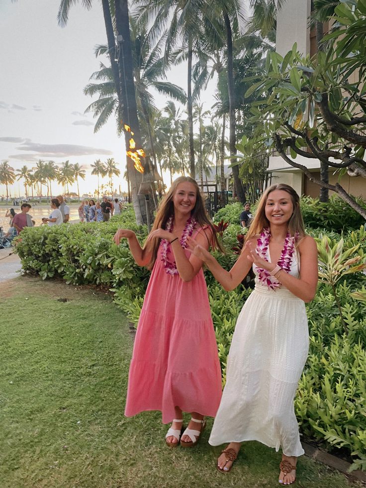 two girls standing in front of some bushes and palm trees with their hands up to the camera