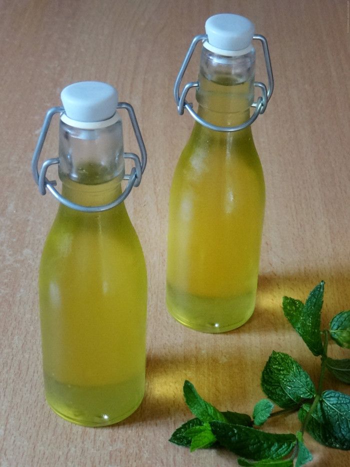 two bottles filled with liquid sitting on top of a wooden table next to mint leaves