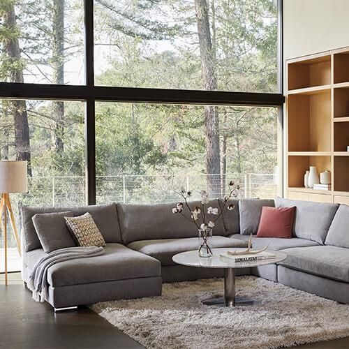 a living room filled with lots of furniture next to a large glass wall window on top of a hard wood floor