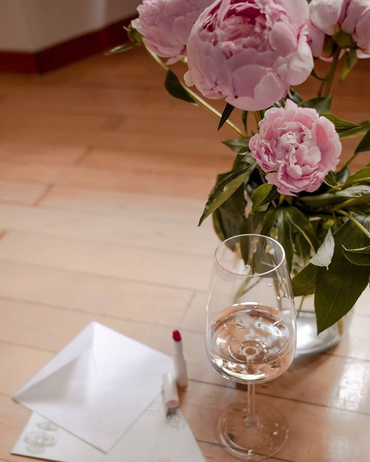 pink flowers in a vase and a glass of wine on a table with envelopes