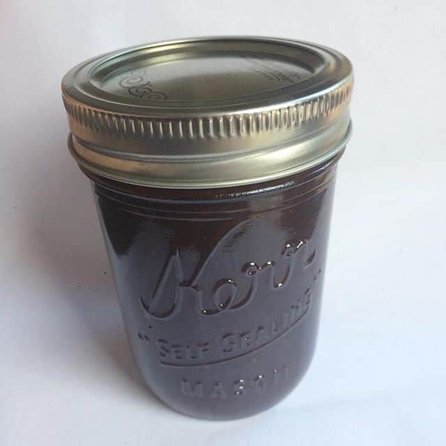 a mason jar filled with lots of dark colored liquid sitting on top of a white table