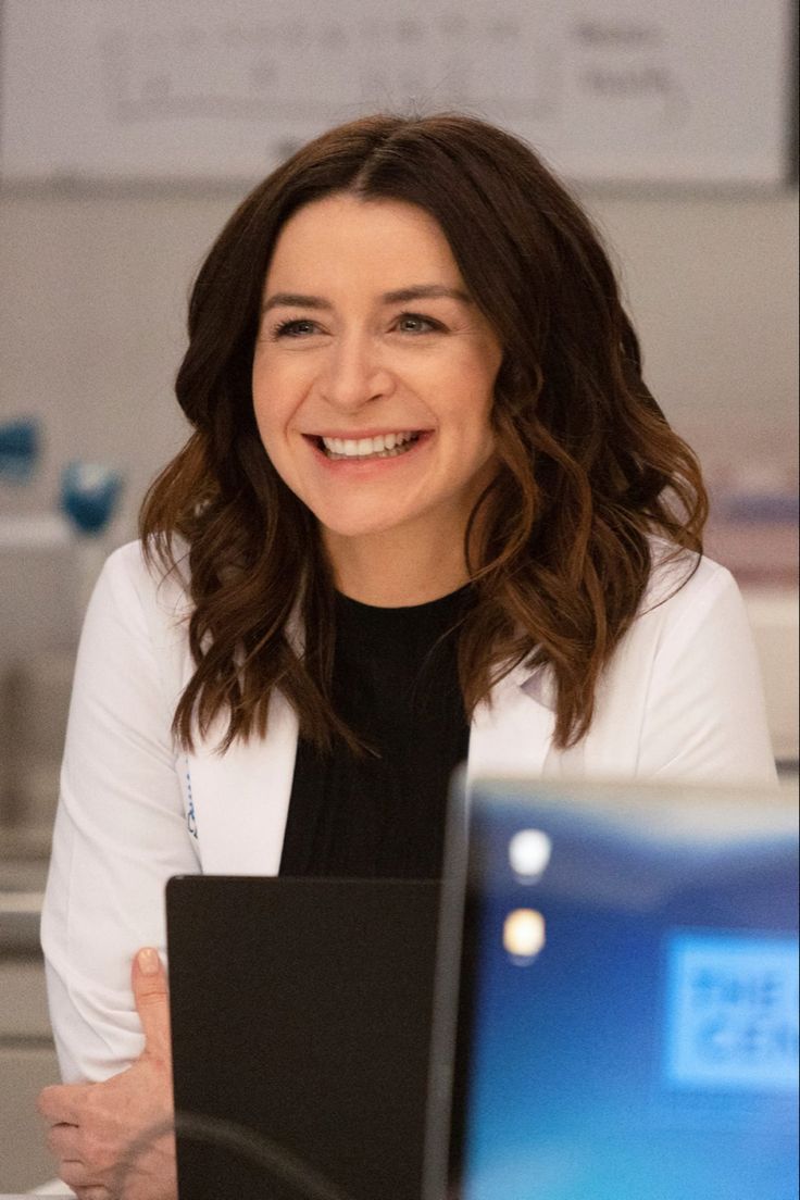 a woman sitting in front of a laptop computer smiling at the camera with her arms crossed