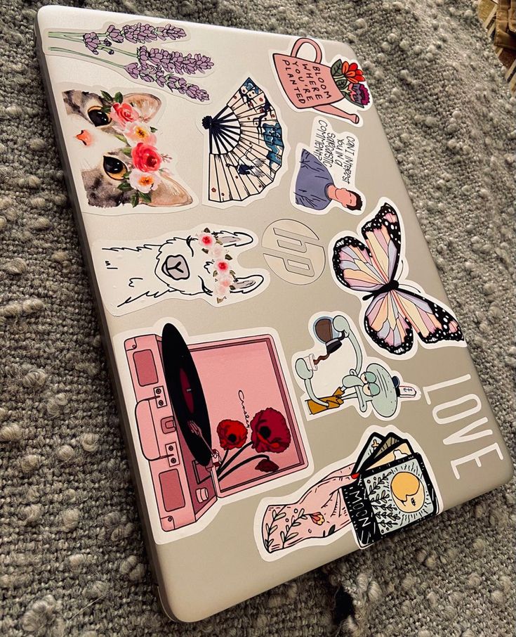 a laptop covered in stickers sitting on top of a carpet next to a pillow