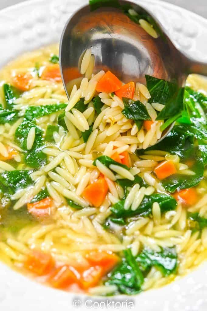 a white bowl filled with pasta and spinach on top of a table next to a spoon