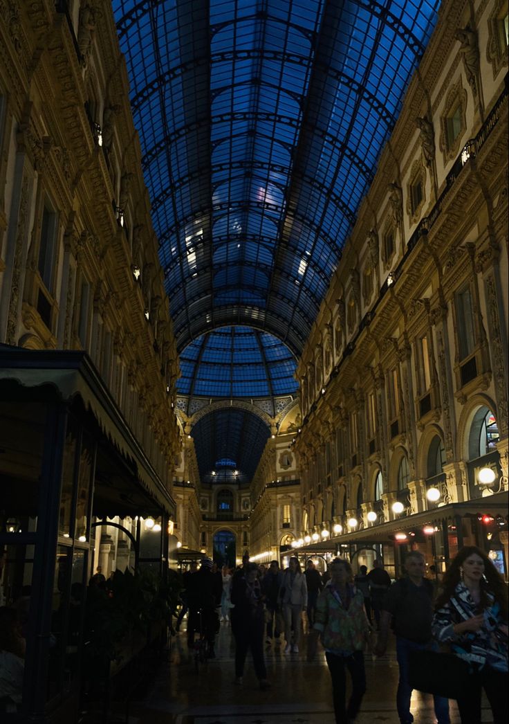 an indoor shopping mall with many people walking around the area and lights on either side