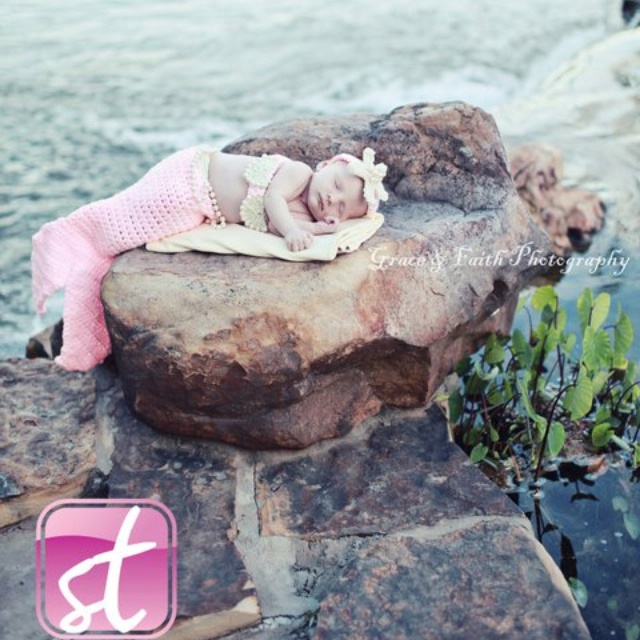 a baby laying on top of a rock next to the ocean