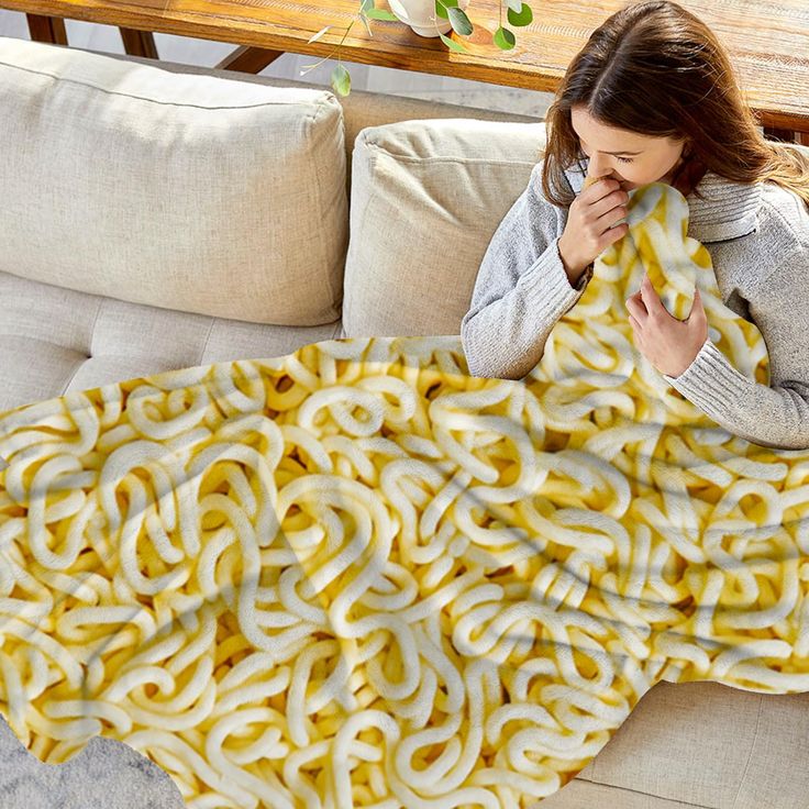 a woman covers her face with a giant blanket made out of yellow rings on a couch