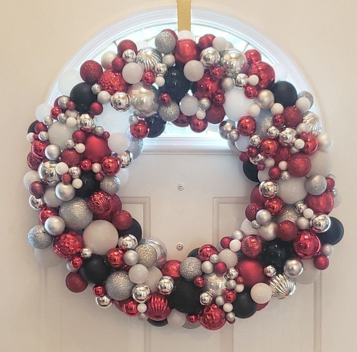 a christmas wreath hanging on the front door with ornaments around it and an ornament in the middle