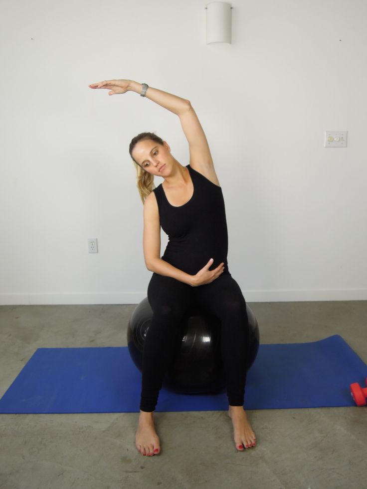 a woman is sitting on an exercise ball and stretching her arms with one hand while holding the other