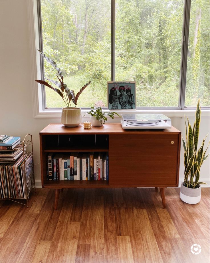 a wooden table with books and plants on it in front of a large window that overlooks the woods