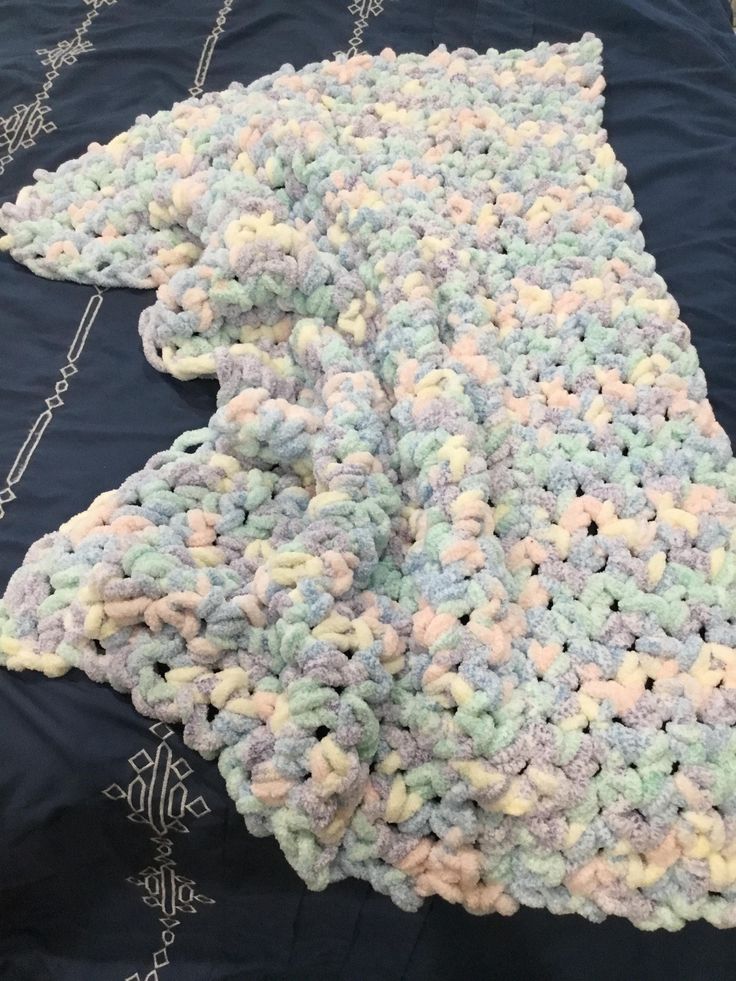 a crocheted blanket laying on top of a bed next to a blue comforter