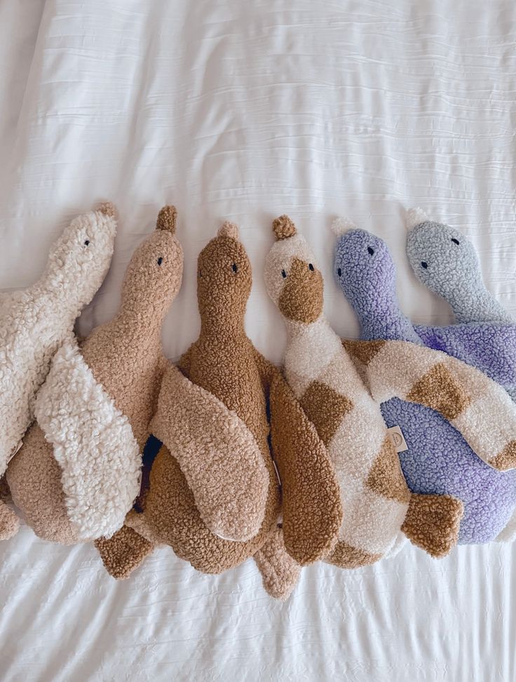 five stuffed animals lined up in a row on a white bed with the covers pulled down