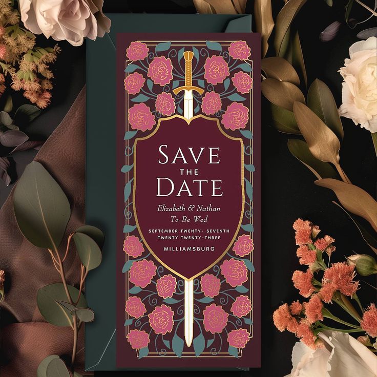 an ornate save the date card surrounded by flowers and greenery on a black background