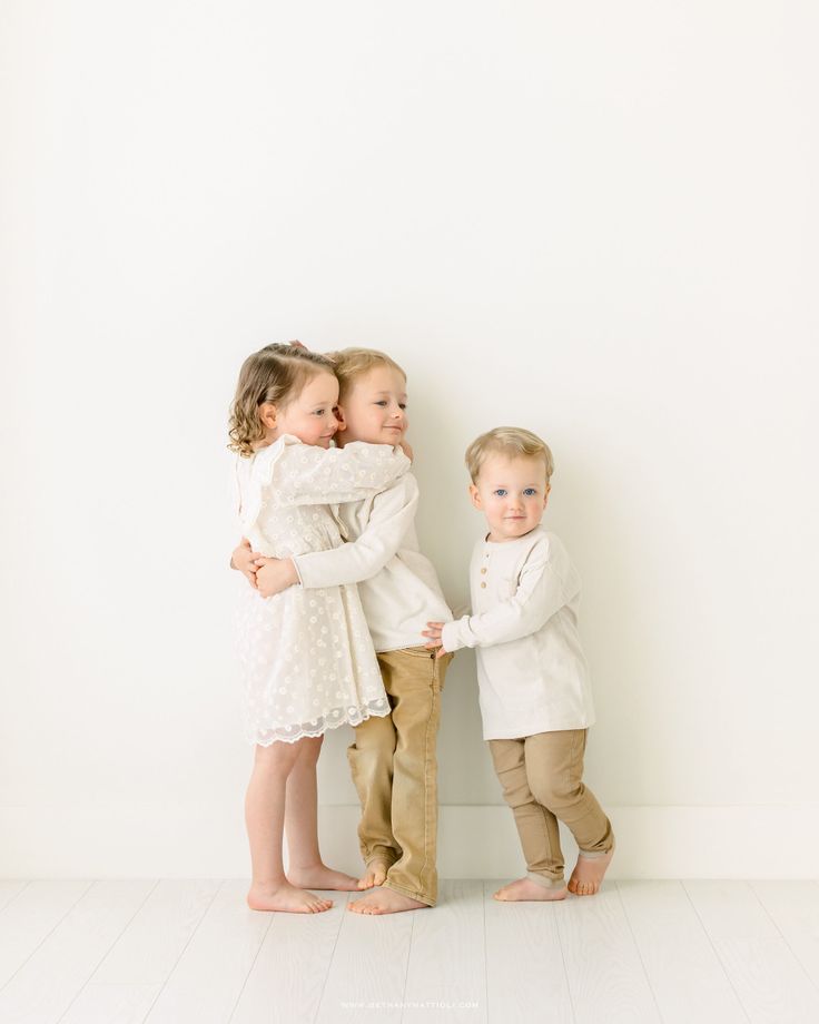 two little kids hugging each other in front of a white wall