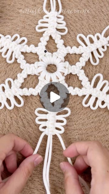 someone is making a snowflake out of white yarn and thread with their hands