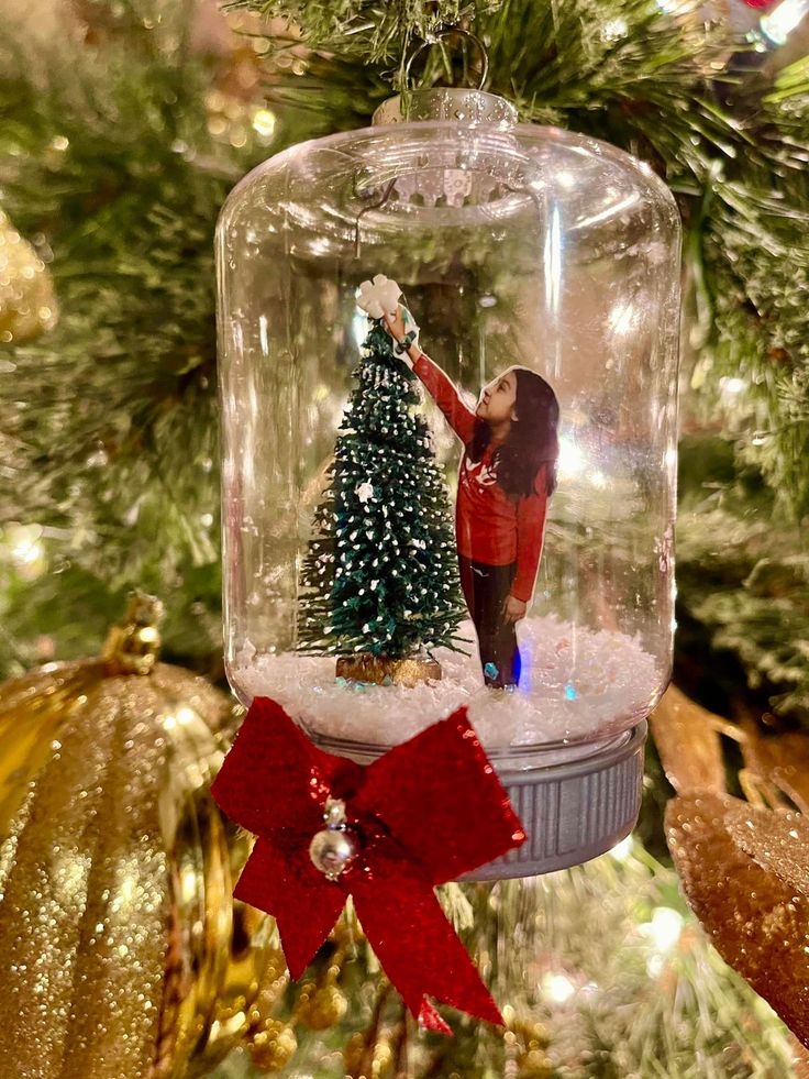 a snow globe ornament with a christmas tree in it and a red bow