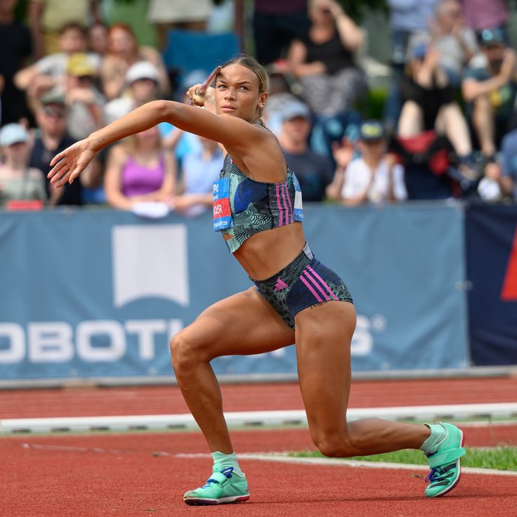 a woman is running on a track in front of an audience with her arm outstretched