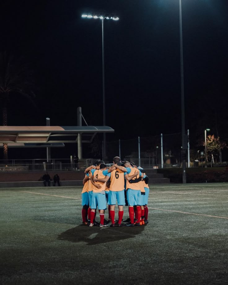 a group of soccer players huddle together on the field in front of stadium lights