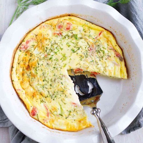 an omelet in a white dish with a piece missing from it and a fork on the side