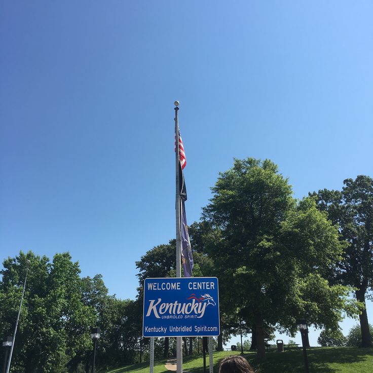 a woman is standing in front of a sign for the kentucky state flag and an american flag