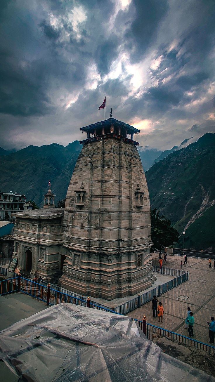 an old building with a flag on top in the middle of mountains and people standing around it