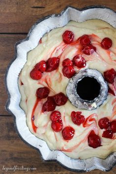 a cake with white frosting and red cherries on top, sitting on a wooden table