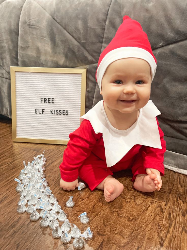 a baby dressed as elf sitting on the floor next to a sign that says free elf kisses