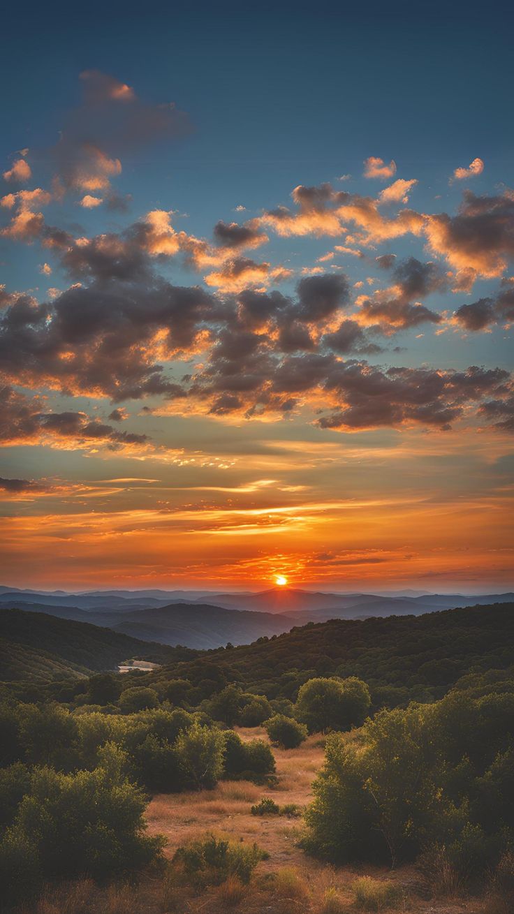 the sun is setting over some hills with trees and bushes in the foreground,