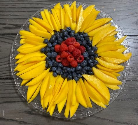 a sunflower with berries and blueberries in the center on a clear platter