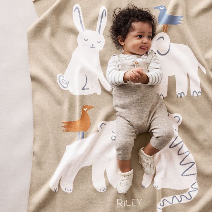 a baby laying on top of a blanket next to a pillow with animals on it