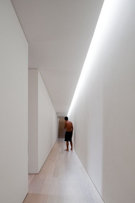 a man walking down a hallway between two white walls with light coming in from the ceiling