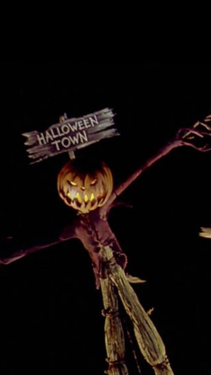 a scarecrow holding a sign that says halloween town