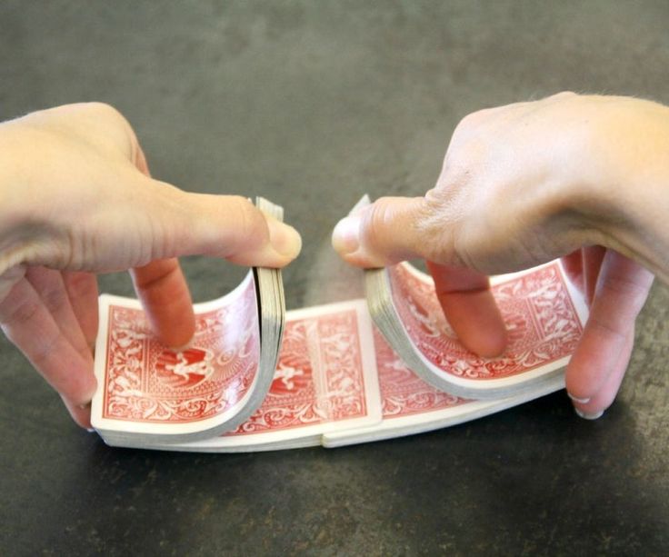 two hands reaching for playing cards with their fingers on the top one and bottom one